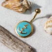 Piercing nombril doré à ancre marine sur fond bleu